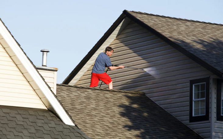 man using a pressure washing on house exterior and roof